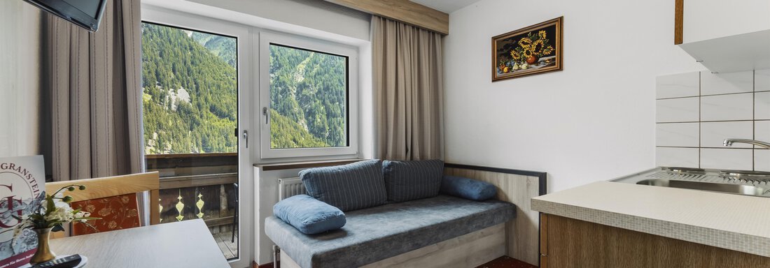 Ein gemütliches Zimmer mit einem Sofa und einer kleinen Küchenzeile. Durch das Fenster ist eine schöne Aussicht auf die Berge zu sehen. - Gasthof Granstein - Sölden