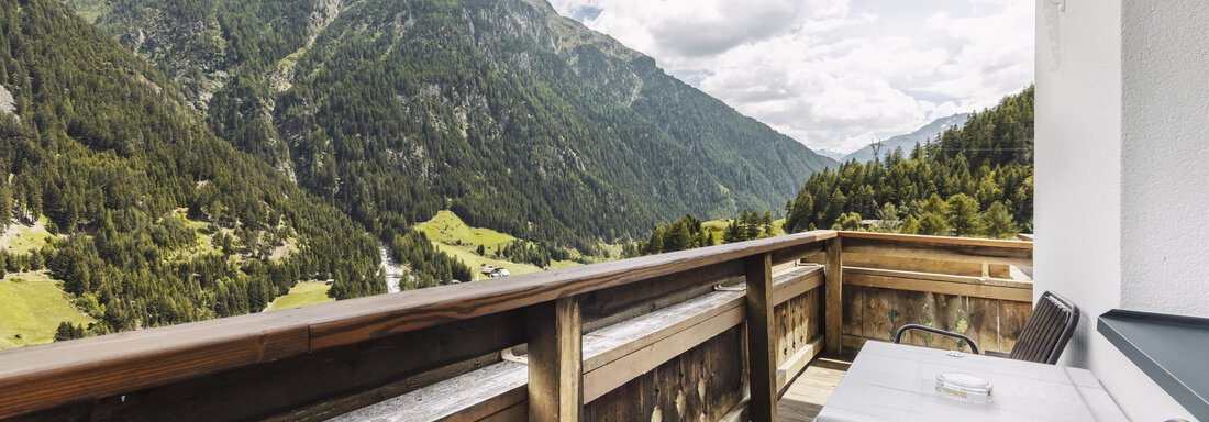 Ein Balkon mit Holzgeländer und zwei Stühlen bietet einen atemberaubenden Blick auf die Berge. Der Himmel ist bewölkt und die Landschaft ist grün und bergig. - Gasthof Granstein - Sölden