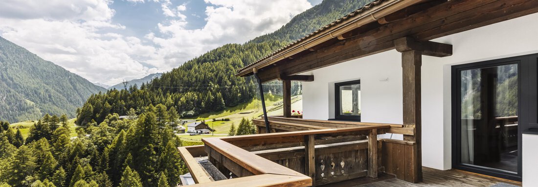 Eine moderne Terrasse mit Holzgeländer und Blick auf grüne Berge. Der Himmel ist teilweise bewölkt und lädt zum Entspannen ein. - Gasthof Granstein - Sölden