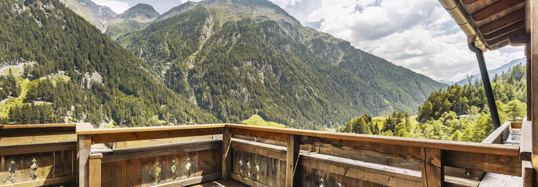 Eine Holzterrasse mit Blick auf majestätische Berge und grüne Wälder. Der Himmel ist bewölkt und es herrscht eine ruhige Atmosphäre. - Gasthof Granstein - Sölden