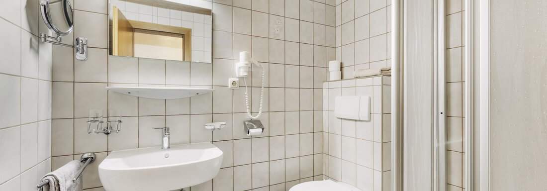 Ein modernes Badezimmer mit weißen Fliesen und einer Duschkabine. Es enthält ein Waschbecken, eine Toilette und einen Spiegel. - Gasthof Granstein - Sölden