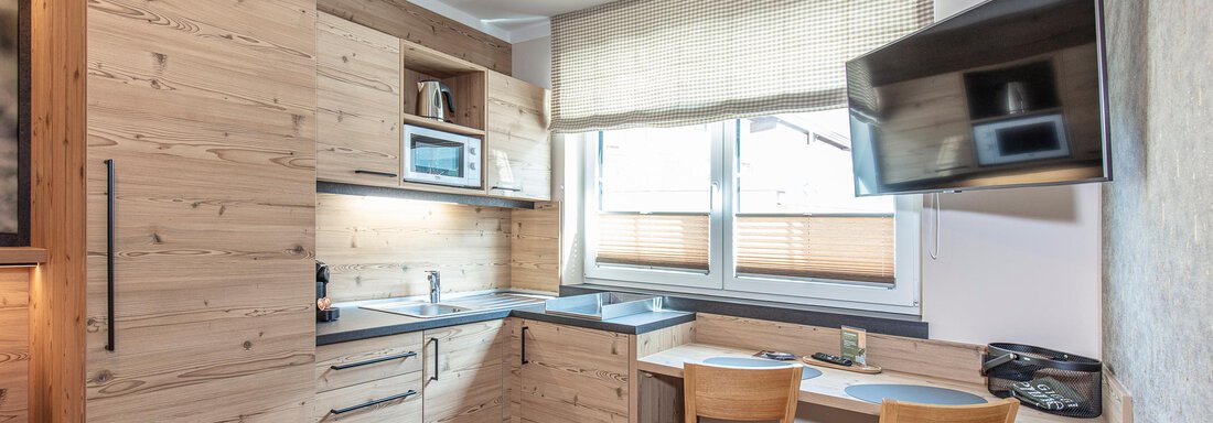 A modern kitchen with wooden cabinets and a small dining area. There is a microwave, a refrigerator, and a television on the wall. - GIGGI Tenne Studios - Sölden