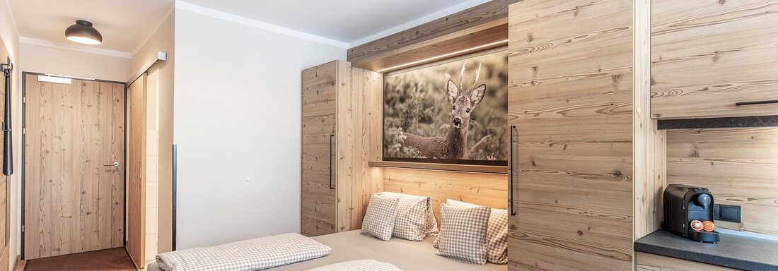 A modern bedroom with wooden paneling and a double bed. On the wall hangs a picture of a deer, creating a cozy atmosphere. - GIGGI Tenne Studios - Sölden
