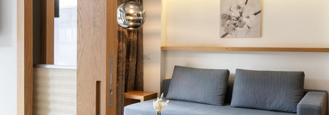 A modern living room with a gray sofa and a small table.  
On the wall hangs a piece of artwork and there is stylish lighting. - Glanz & Glory Hotel - Sölden
