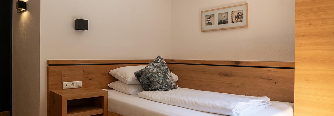 A simple room with a single bed, wooden elements, and a small table. The walls are bright and there are some modern decorations. - Glanz & Glory Hotel - Sölden