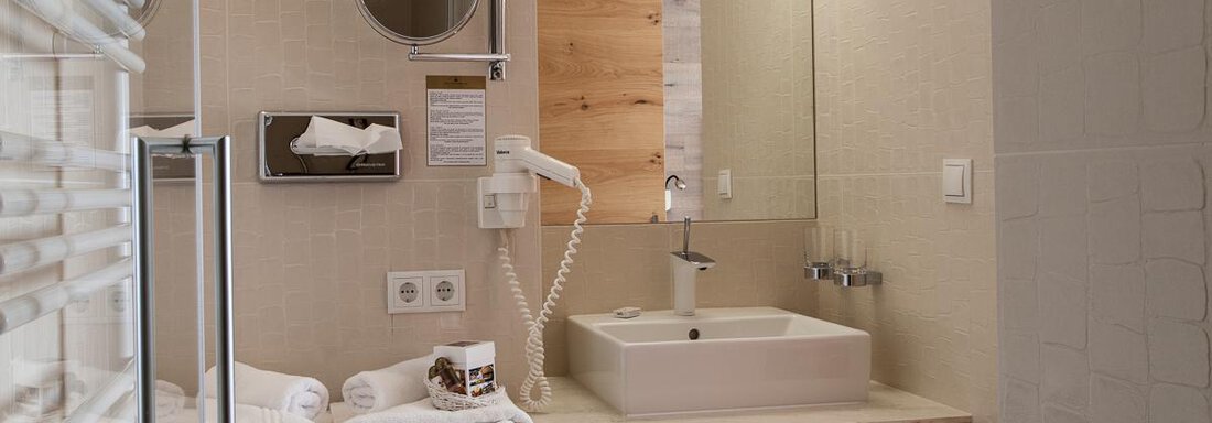 A modern bathroom with a sink on a wooden shelf. There are towels, a mirror, and bright, neutral colors. - Glanz & Glory Hotel - Sölden