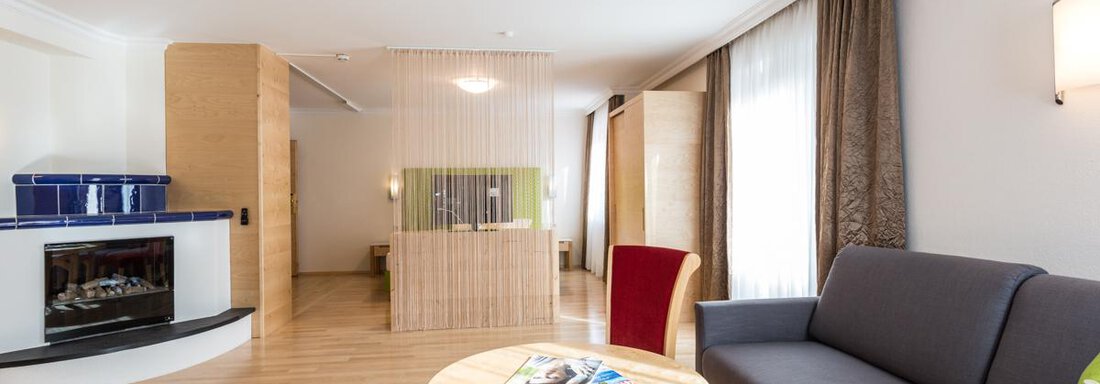A modern living room with a cozy sofa, a round table, and warm wooden flooring. Large windows let in plenty of daylight and give the room an inviting atmosphere. - Glanz & Glory Hotel - Sölden
