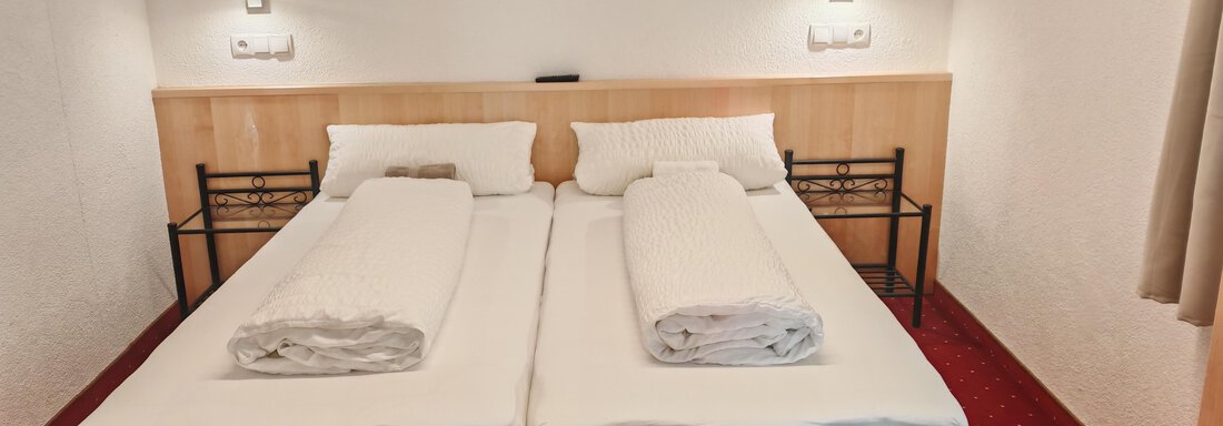 Ein einfaches Zimmer mit zwei Einzelbetten und sauberen Bettwäsche. Die Wände sind hell, und der Boden ist mit rotem Teppich ausgelegt. - Haus der Bergfreunde - Sölden
