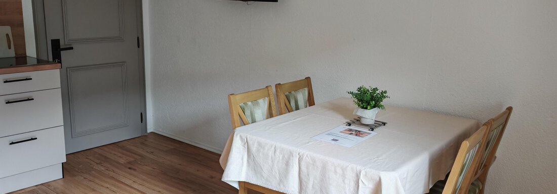 Ein kleiner Esstisch mit vier Stühlen in einem hellen Raum. An der Wand hängt ein Fernseher und es gibt einen Holzfußboden. - Haus der Bergfreunde - Sölden
