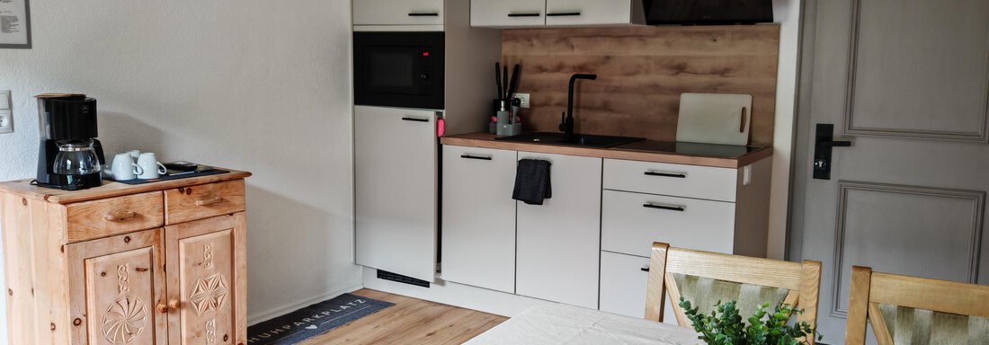 Eine moderne Küche mit Holzfußboden und weißen Schränken. Der Tisch ist mit einem hellen Tuch und einer Pflanze dekoriert. - Haus der Bergfreunde - Sölden