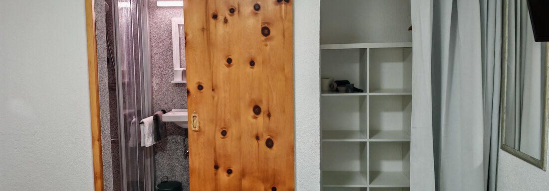 Ein einfaches Zimmer mit einem Bett und einem Kasten. Im Hintergrund ist ein Badezimmer mit einer Dusche sichtbar. - Haus der Bergfreunde - Sölden
