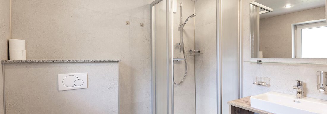 A modern bathroom with a shower and a sink. The walls are in neutral tones and there is a large mirror surface. - Haus Falkner Ignaz - Sölden