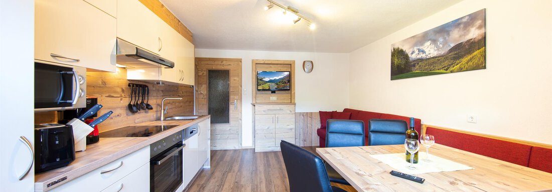 A modern kitchen with wooden flooring and white furniture. A dining table with chairs and a cozy seating area are visible. - Haus Falkner Ignaz - Sölden