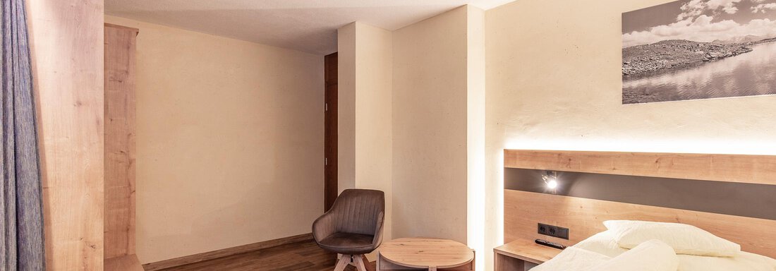 Ein moderner Hotelraum mit einem Einzelbett, einem Stuhl und einem kleinen Tisch. Die Wände sind hell und der Boden aus Holz. - Haus Manfred - Sölden