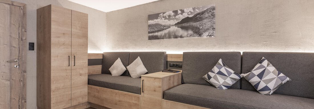 Ein moderner Wohnraum mit gemütlichen Sitzgelegenheiten und Kissen. Die Wände sind in neutralen Tönen gehalten und es gibt Holzdetails. - Haus Manfred - Sölden