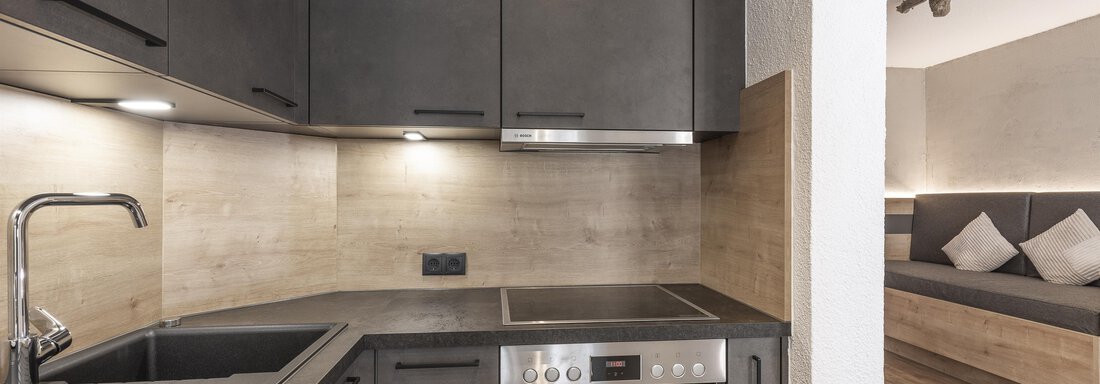 Eine moderne Küchenzeile mit schwarzen Schränken und Edelstahlgeräten. Der Raum wirkt hell und einladend mit Holzfelementen. - Haus Manfred - Sölden
