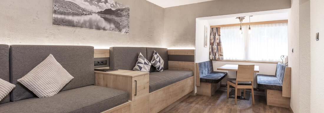Ein modernes Wohnzimmer mit gemütlichen Sitzgelegenheiten in Grau und Holz. Es gibt einen Essbereich mit einem Tisch und Stühlen sowie viel natürliches Licht. - Haus Manfred - Sölden