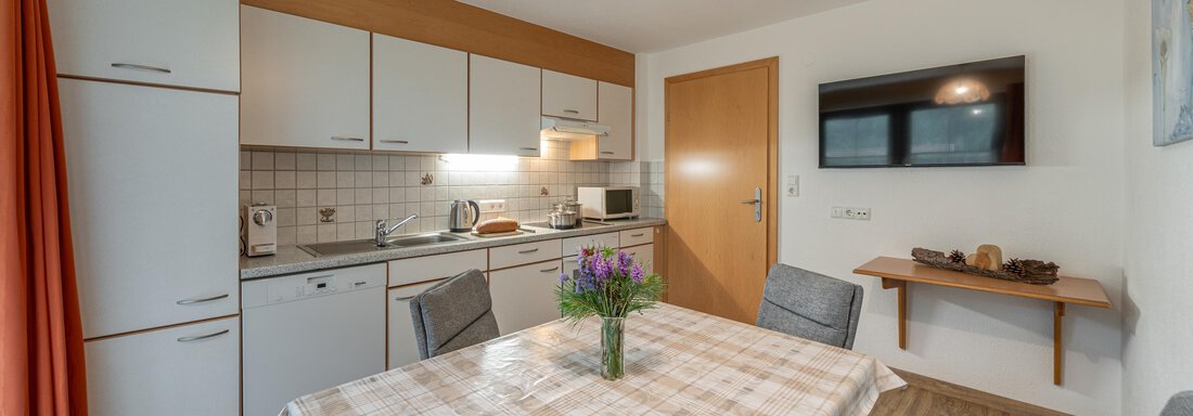 A modern kitchen with a dining table and chairs. The kitchen is well-equipped and has a television on the wall. - Haus Nicola - Sölden