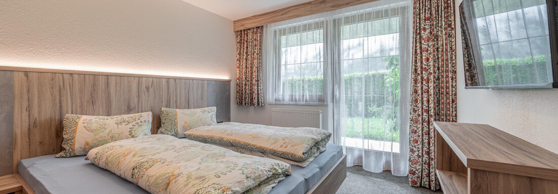A modern bedroom with two beds and a bright color scheme. Large windows provide plenty of daylight and a view outdoors. - Haus Nicola - Sölden