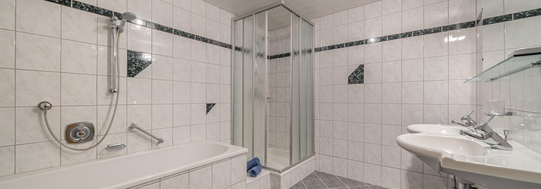 A modern bathroom with a bathtub and a shower. White tiles and a bright, clean atmosphere characterize the space. - Haus Nicola - Sölden