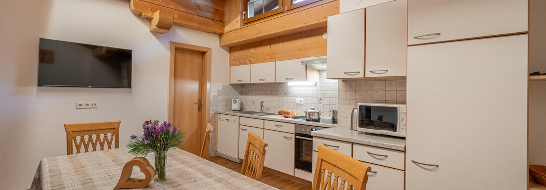 A modern kitchen with wooden ceilings and a large dining table. In the corner stands a vase with fresh flowers. - Haus Nicola - Sölden