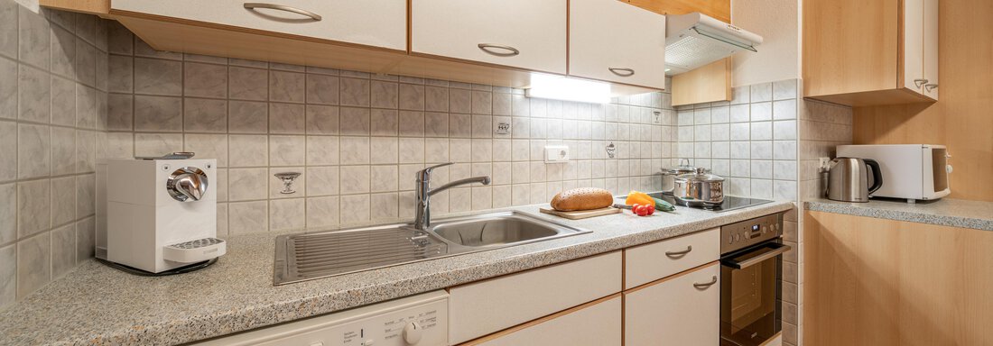 A modern kitchen with light wooden elements and white furniture. The room is well equipped with appliances such as a stove, a microwave, and a large sink. - Haus Nicola - Sölden