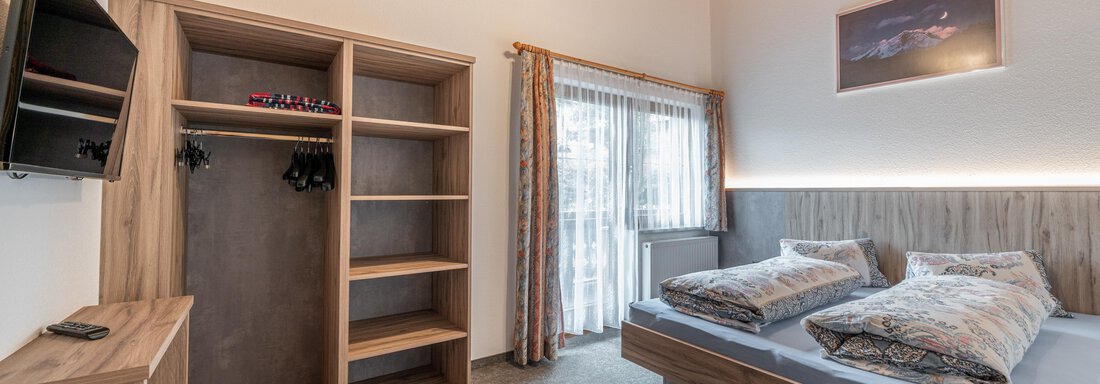 A modern room with wood and sand tones. There is a double bed, a television, and a wardrobe. - Haus Nicola - Sölden