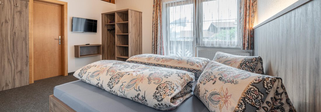 A modern bedroom with a large bed and pretty pillows. The wooden beam ceiling and the windows create a cozy atmosphere. - Haus Nicola - Sölden