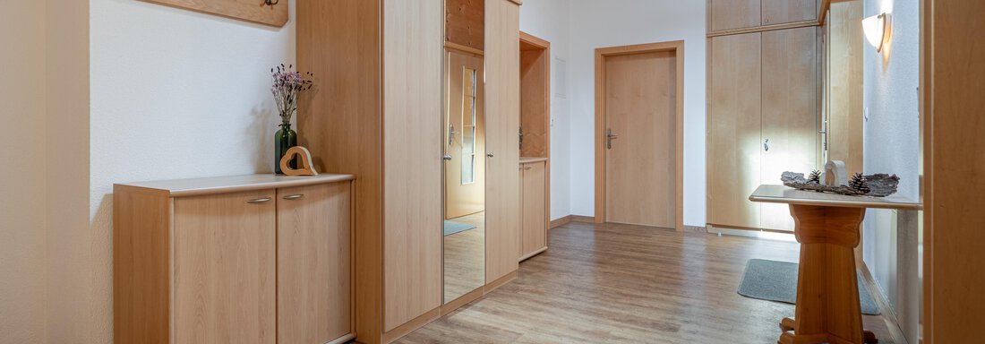 A modern, bright entrance area with wood paneling. There are cabinets, a coat rack, and a table that create an inviting impression. - Haus Nicola - Sölden