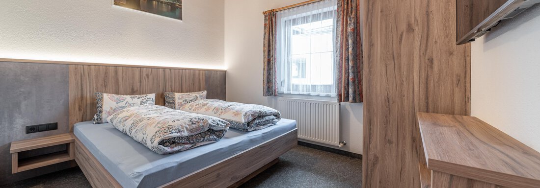 A modern bedroom with a large double bed and wooden paneling. It also has a television and a cozy wardrobe. - Haus Nicola - Sölden