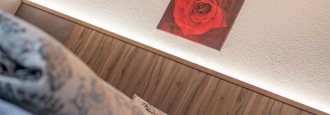 A cozy room with a comfortable pillow and a piece of artwork depicting a red rose on the wall. The warm lights create an inviting atmosphere. - Haus Nicola - Sölden