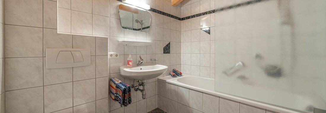 A modern bathroom with tiles and a wooden ceiling. It features a bathtub, a sink, and a shower. - Haus Nicola - Sölden