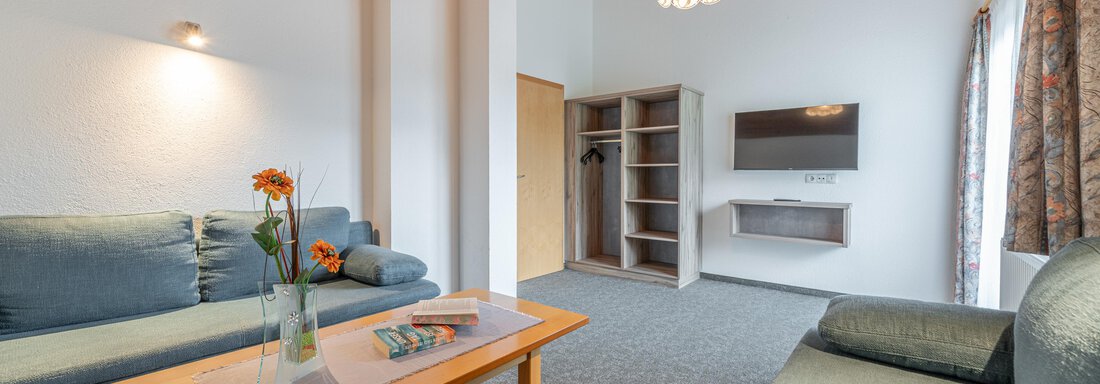 A cozy living room with blue sofas and a wooden table. On the wall hang curtains and there is a TV set as well as a floor lamp. - Haus Nicola - Sölden