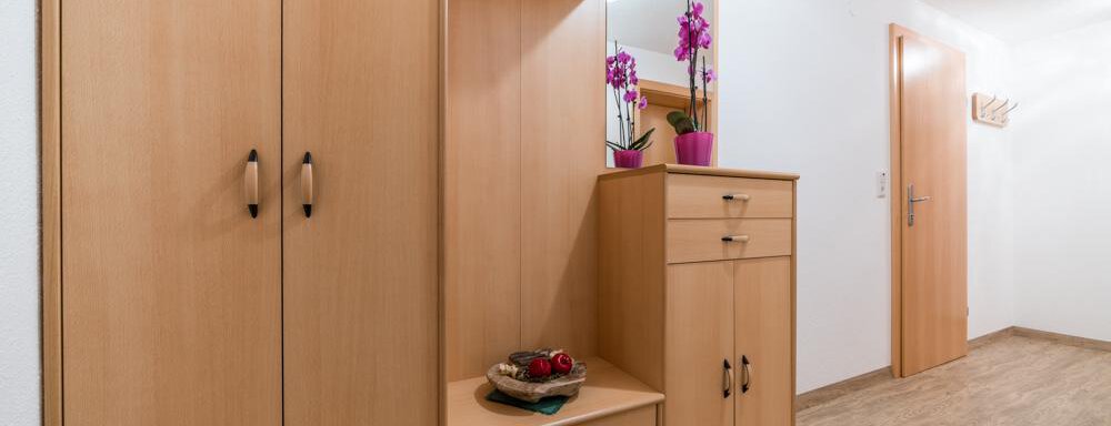 A bright hallway with a modern wooden coat rack. On a table, there are floral decorations and a few decorative items. - Haus Nicola - Sölden
