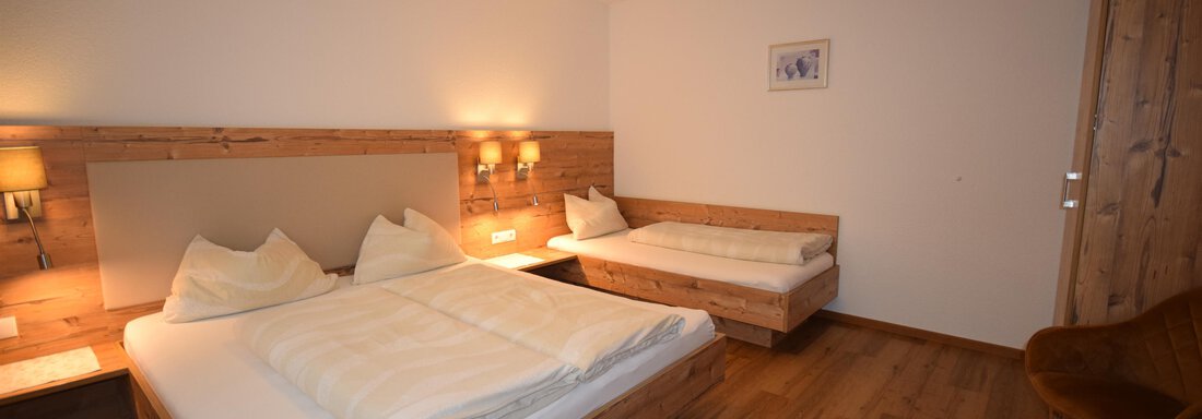A cozy bedroom with two beds and a single sleeping area. The walls are light, and the floor is made of wood, creating a warm atmosphere. - Haus Romana - Sölden