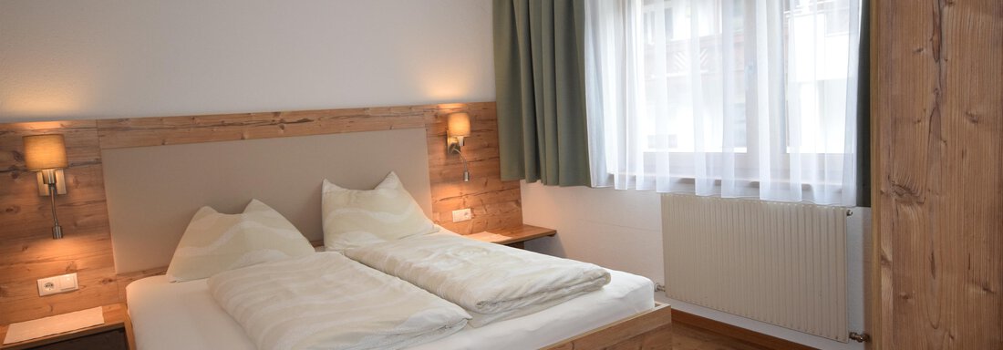A cozy bedroom with a double bed and wooden details. Large windows let in plenty of daylight. - Haus Romana - Sölden