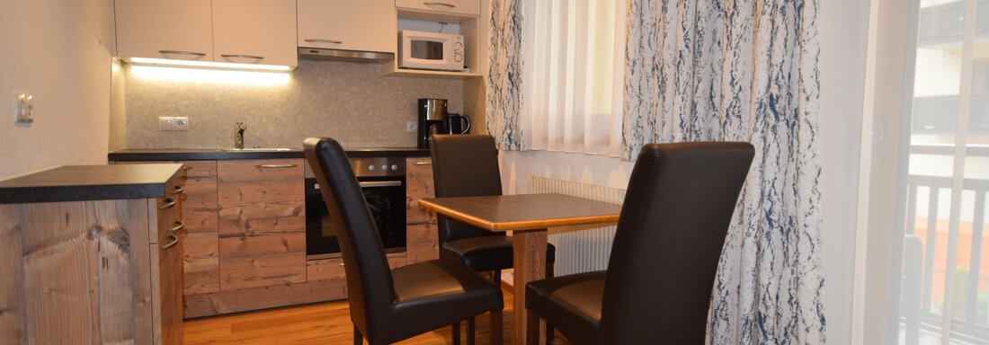 Eine moderne Küche mit Holzmöbeln und einem Tisch für vier Personen. Das Zimmer hat viel Licht durch die Fenster und eine gemütliche Atmosphäre. - Haus Romana - Sölden