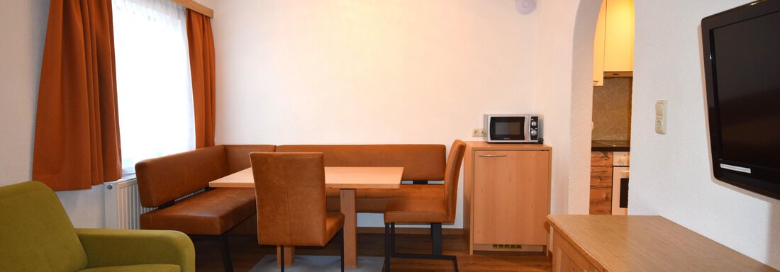 Ein gemütlicher Wohnraum mit einem grünen Sofa und einem Essbereich. Die Wände sind hell und die Fenster mit Vorhängen dekoriert. - Haus Romana - Sölden