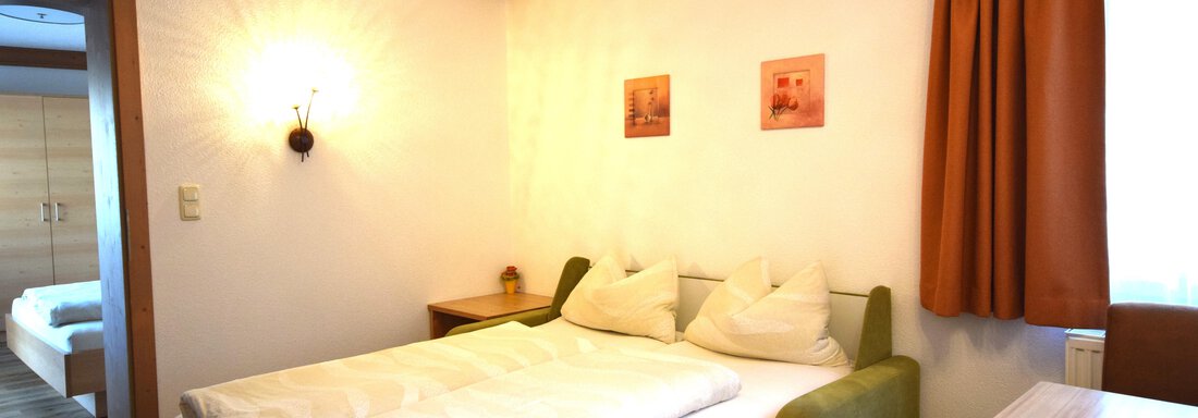 Ein gemütliches Schlafzimmer mit einem Doppelbett und zwei Kissen. Die Wände sind hell, und es gibt orangefarbene Vorhänge sowie einige dekorative Bilder. - Haus Romana - Sölden