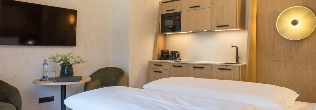 Ein modernes Zimmer mit zwei Betten und einer kleinen Küchenzeile. Eine gemütliche Atmosphäre mit einem Fernseher und einem kleinen Tisch. - Hotel Alpina - Sölden