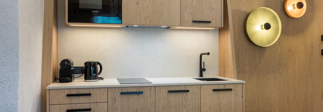 Eine moderne Küche mit Holzschränken und einer Mikrowelle. Es gibt eine Kaffeemaschine und eine Spüle in einem gemütlichen Wohnraum. - Hotel Alpina - Sölden