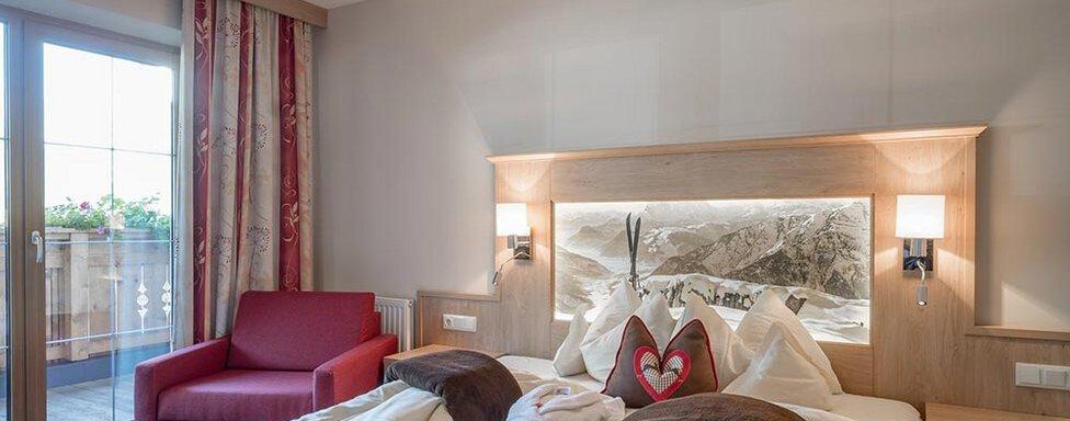 Schlafzimmer Hotelappartement | © Hotel Elisabeth (CC C) Ein gemütliches Schlafzimmer mit einem großen Bett und eleganter Holzmöbel. Ein roter Sessel und ein Balkon mit Fenster sorgen für eine helle Atmosphäre. - Hotel Elisabeth - Sölden