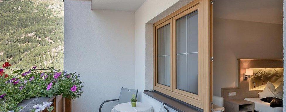 Ein gemütlicher Balkon mit zwei Stühlen und einem kleinen Tisch. Im Hintergrund sind blühende Pflanzen und Berge zu sehen. - Hotel Elisabeth - Sölden