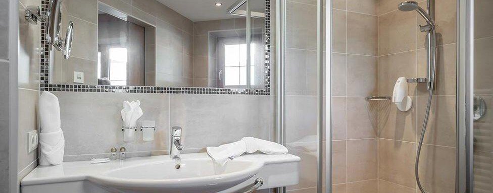 Ein modernes Badezimmer mit Dusche und großen Spiegeln. Die hellen Fliesen und Handtücher sorgen für einen sauberen Eindruck. - Hotel Elisabeth - Sölden