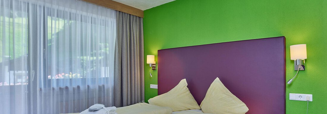 Ein modernes Schlafzimmer mit einem großen Doppelbett und bunten Wänden. Viel Licht durch die Fenster und frische Annehmlichkeiten sind sichtbar. - Hotel Erhart - Sölden