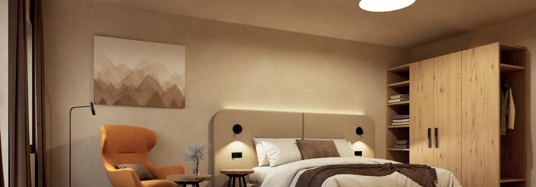 Das Bild zeigt ein modernes Schlafzimmer mit einem großen Bett und einem gemütlichen Sessel. Die Wände sind in neutralen Tönen gehalten, und es gibt einen Holzschrank im Hintergrund. - Hotel Garni Hainbacherhof - Sölden