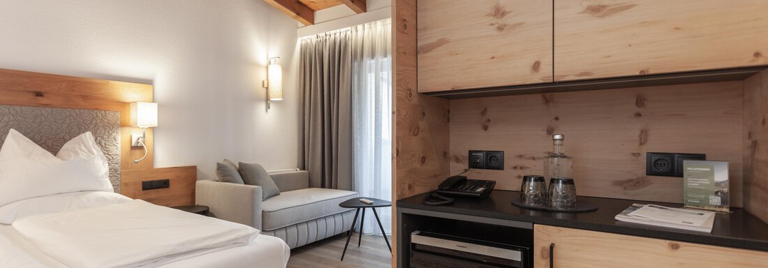 A modern hotel room with a cozy bed and a small kitchenette. The wood paneling and soft lighting create an inviting atmosphere. - Hotel Hubertus - Sölden