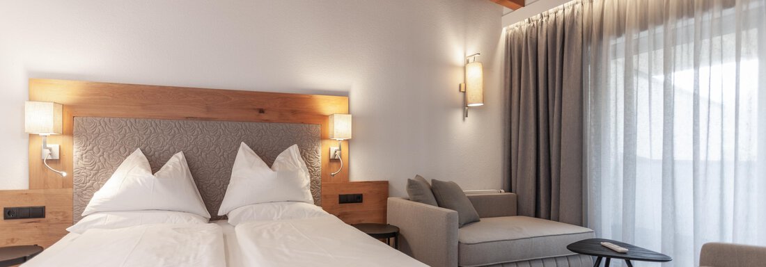 A modern hotel room with two beds and a cozy seating area. Large windows let in plenty of light and offer a view outside. - Hotel Hubertus - Sölden