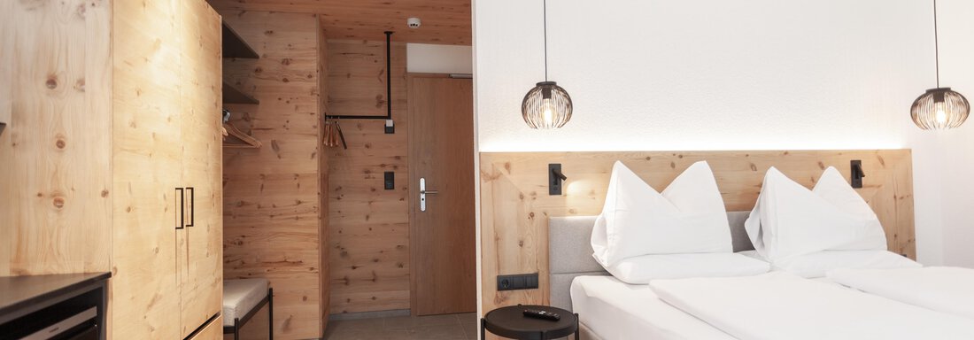 A modern hotel room with two beds, wooden paneling, and stylish lamps. The space is bright and minimally furnished. - Hotel Hubertus - Sölden