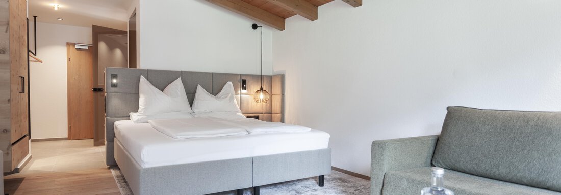 A modern room with a large bed and a cozy sofa. The wooden ceiling gives the space a warm atmosphere. - Hotel Hubertus - Sölden
